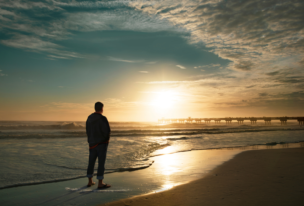 Man stands alone watching sunrise on a beach in California.