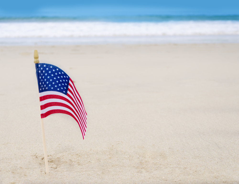 An American flag stands in the sand on the beach.